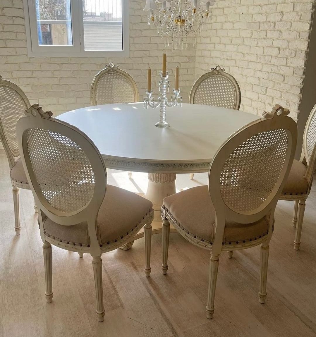 A French white round dining set with six chairs featuring beige upholstery and cane backrests, centered around a decorative table with a glass top.