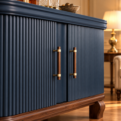 A close-up of a navy blue cabinet with vertically fluted doors, warm wood handles, and a dark wood base, shown in a styled interior with a lamp in the background.