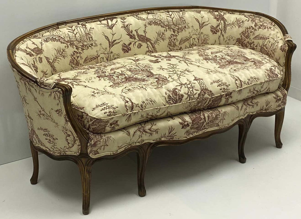 Antique sofa with beige fabric upholstery featuring floral printed motifs, with a curved silhouette and wooden legs.