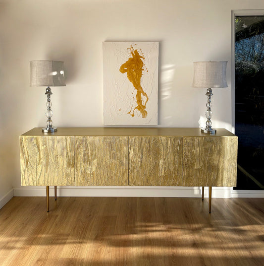 Gold sideboard with two lamps and a painting in a room.