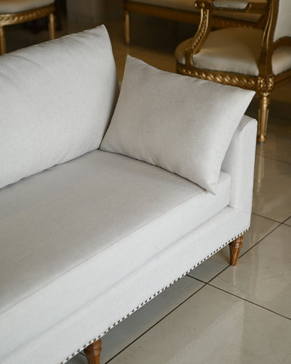 White sofa with gold legs in a room with tiled floor and wooden furniture.