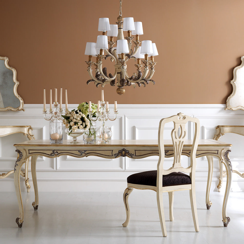 Dining room with ornate table, chairs, and chandelier against a peach wall.