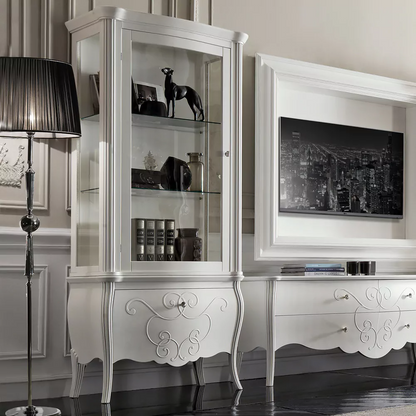 A white display cabinet with glass shelves and patterned drawer, placed in a room with a light interior.