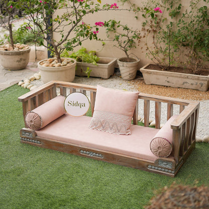 Wooden outdoor bench with pink cushions and 'Sidqa' branding in a garden setting.